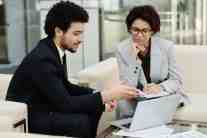 Two professionals discussing strategy while reviewing documents on a laptop