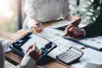 Close-up of hands pointing at charts and graphs on a table, with a laptop and calculator visible.
