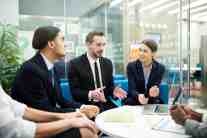 A group of professionals in business attire engaged in a discussion around a table in a modern office setting.